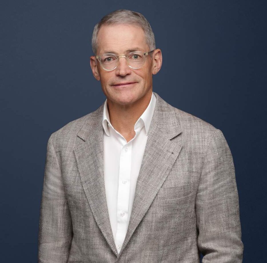 Michael Fisch wearing a gray blazer and white shirt against a dark blue background